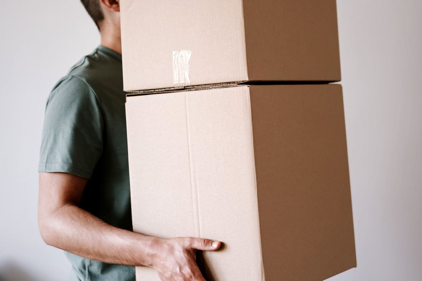 Deux cartons empilés portés à bout de bras dans une pièce vide.
