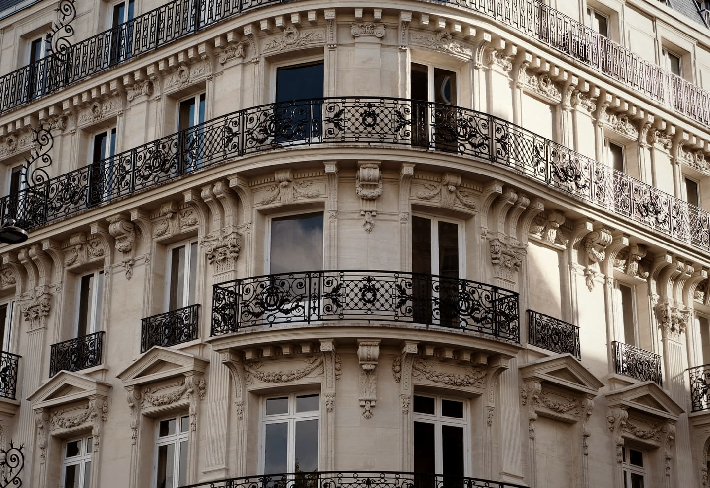 Façade haussmannienne à l'angle d'une rue : pierre de taille, balcons filants et ferronnerie ouvragée sur trois étages.
