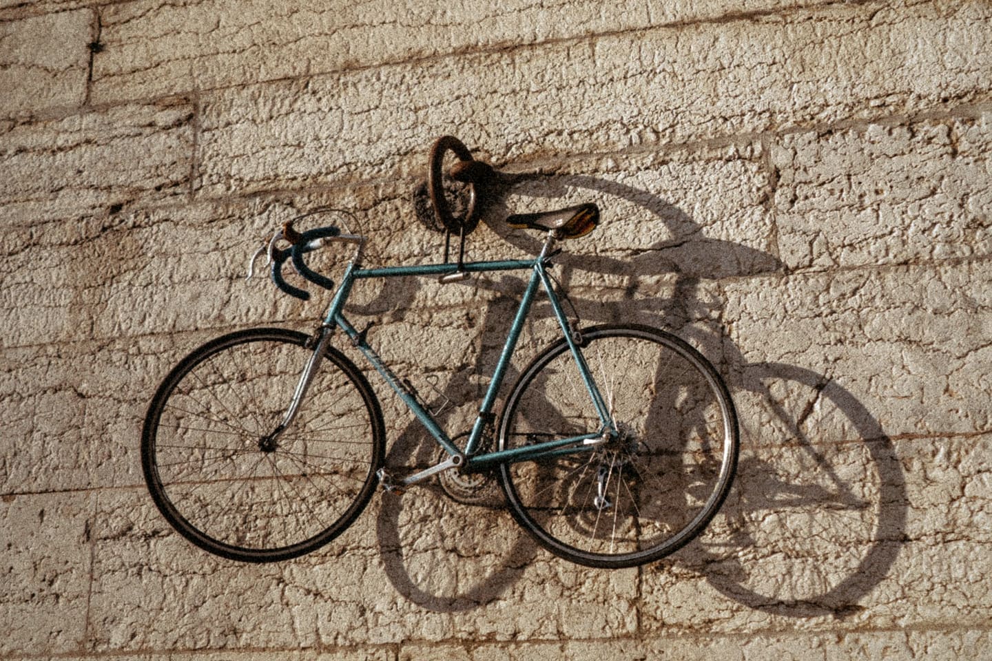 Vélo de route suspendu à un crochet mural, son ombre portée sur la pierre.